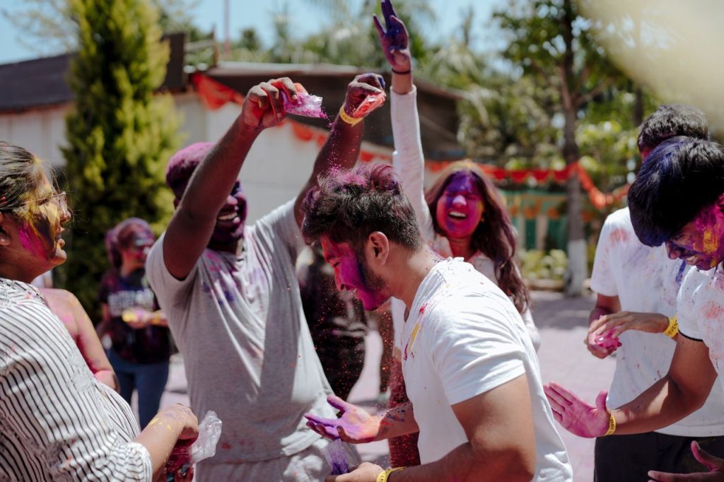 Group of friends joyfully celebrating Holi with colored powders outdoors in daylight.